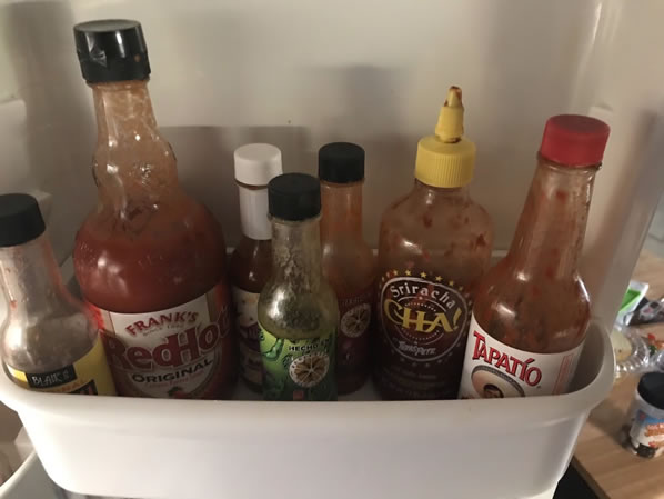 Penny's collection of seven different hot sauces on their dedicated refrigerator shelf